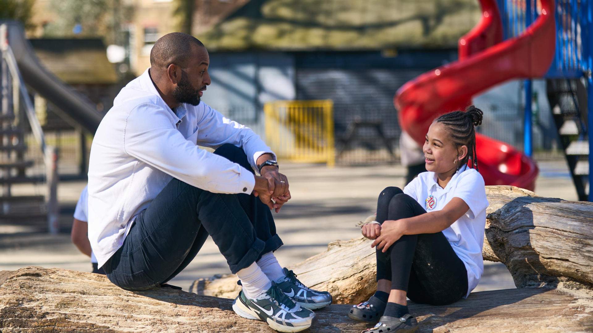 A teacher and a student sit talking to each other in the playground