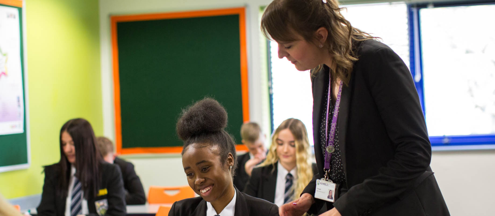A classroom of students sitting at desks with a teacher talking to a student