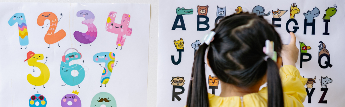 A young child with hair in bunches is pointing at a poster of the alphabet