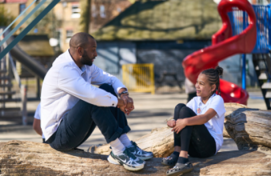 A teacher and a student sit talking to each other in the playground